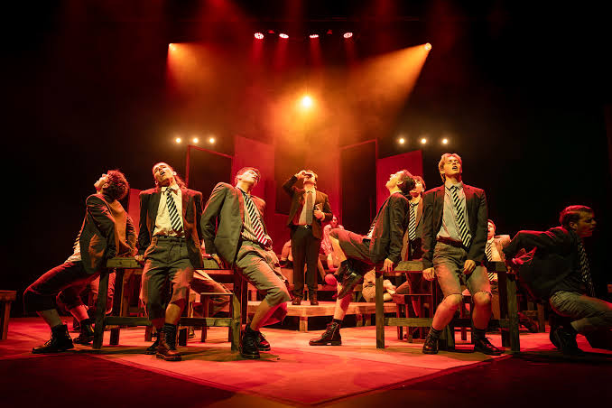 A full musical theatre company performing on a tiered set